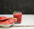 Slices of ripe watermelon on a plate and red watermelon juice in a glass on a wooden white background, and a black wall - side Royalty Free Stock Photo