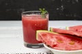 Slices of ripe watermelon on a plate and red watermelon juice in a glass on a wooden white background, and a black wall - side Royalty Free Stock Photo