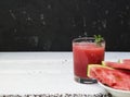 Slices of ripe watermelon on a plate and red watermelon juice in a glass on a wooden white background, and a black wall Royalty Free Stock Photo