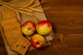 Slices of rye bread, three apples, ears of wheat on sacking, wooden table Royalty Free Stock Photo