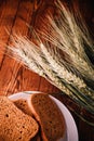 Slices of rye wholegrain bread on white plate, wheat ears on wooden boards background, rustic kitchen table. Homemade bread,