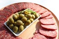 Slices of salami pepperoni and green pickled olives on round wooden cut board on white background. Top view Royalty Free Stock Photo