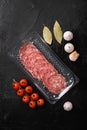 Slices of sausage salami in vacuum package, on black dark stone table background, top view flat lay Royalty Free Stock Photo