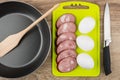 Slices of smoked sausage, eggs on cutting board, frying pan Royalty Free Stock Photo