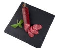 Slices of smoked sausage and a sausage stick with fresh basil on a black slate cutting board Royalty Free Stock Photo