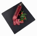 Slices of smoked sausage and a sausage stick with fresh herbs on a black cutting board Royalty Free Stock Photo