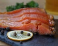 slices of smoked trout lie on a black basalt board next to a circle of lemon and spices