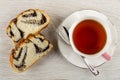 Slices of sweet bun with poppy, cup of tea, spoon on saucer on table. Top view Royalty Free Stock Photo
