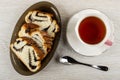 Slices of sweet bun with poppy in dish, cup of tea on saucer, spoon on wooden table. Top view Royalty Free Stock Photo
