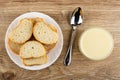 Slices of bun in white plate, spoon, bowl with condensed milk on wooden table. Top view Royalty Free Stock Photo