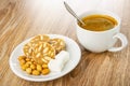 Slices of sweet sausage, fried peanuts, sugar in saucer, spoon in cup with coffee on wooden table