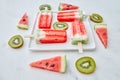 Slices of watermelon and kiwi in the form of a circle and a triangle around a plate with a healthy ice cream lolly in Royalty Free Stock Photo