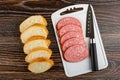 Slices of bread on wooden table, kitchen knife, slices of cervelat on cutting board. Top view Royalty Free Stock Photo