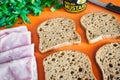 Slices of wholemeal brown bread laid out on a chopping board with ham, rocket and mustard