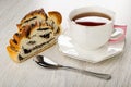 Slices of wicker bun with poppy, cup of tea on saucer, spoon on wooden table Royalty Free Stock Photo