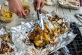 Slicing a BBQ chicken on a aluminum foil with knife and clamp of a charcoal stove
