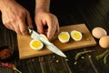 Slicing boiled eggs on the kitchen table. A knife in the hand of a chef cuts an egg for preparing breakfast at the cook room Royalty Free Stock Photo