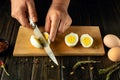 Slicing eggs with a knife in the hands of a man. Low key concept of preparing breakfast from eggs on the kitchen table. View from Royalty Free Stock Photo