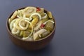 Slicing fermented green tomatoes and cucumbers with onions and pickled peppers in a wooden cup on a gray table. Royalty Free Stock Photo