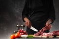 Slicing fresh meat, pork ribs on a background of fresh vegetables and a gray wall with space Royalty Free Stock Photo