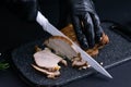 Slicing juicy beef steak by knife in chef hands closeup. Food cooking concept. Dark black background