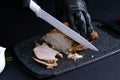 Slicing juicy beef steak by knife in chef hands closeup. Food cooking concept. Dark black background