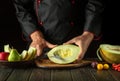 Slicing melon on the kitchen table by the hands of a chef for a fruit menu in a restaurant. Fruit diet concept on dark background Royalty Free Stock Photo