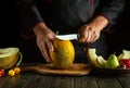 Slicing a melon with a knife in the chef hand for serving a fruity breakfast dish. The idea of a fruit diet in the morning. Work Royalty Free Stock Photo