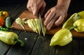 Slicing a ripe bell pepper by the chef's hands before slicing on the kitchen table. Concept of cooking vegetable lecho or Royalty Free Stock Photo