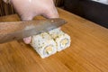 Slicing a roll of tempura maki with a sharp stainless knife on a cutting board. Wearing plastic gloves as health and safety