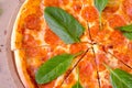 Slicing of salami pizza with spinach leaves on wooden board, close-up top view.