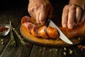 Slicing sausage on a wooden cutting board in the home kitchen by the hands of a cook. The idea of cooking fast food