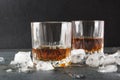 Slightly hot brendy in glasses and ice cubes on gray surface against dark background Royalty Free Stock Photo