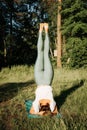 Slim athletic young woman practicing yoga asana, headstand. Rear view of a girl standing on her head on a yoga mat outdoors Royalty Free Stock Photo