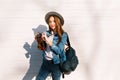 Slim attractive brunette girl in hat with stylish black leather backpack posing holding camera. Gorgeous young long Royalty Free Stock Photo