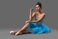Slim ballerina in blue dress sitting on floor in studio