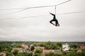 Slim blonde girl balancing high on a slackline against the grey sky and town