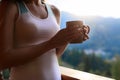 Slim caucasian woman holds cup of tea in her hands at mountain resort. Sports girl with hot coffee mug at wooden balcony Royalty Free Stock Photo