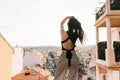 Slim elegant girl with long dark hair enjoying city views from observation deck in morning. Shapely young woman in tank