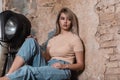 Slim European pretty young woman is resting near a brick wall in a vintage studio. Fashionable girl fashion model in youth casual Royalty Free Stock Photo