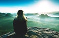 Slim fair hair girl with warm jacket sit on rocky mountain top