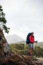 Slim fit girl in sportwear standing with hiking backpack and sticks on the rock