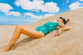 Slim girl in a swimsuit posing on the sand against the background of the sky. Woman lying on the beach.