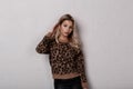 Slim glamorous young woman with long blond curly hair in a stylish leopard sweater in fashionable black leather pants posing in Royalty Free Stock Photo