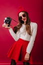 Slim gorgeous woman in red hat and skirt posing with camera. Winsome female photographer in white sweater isolated on