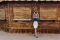 Slim graceful stylish lady fooling around near the wooden stall, touching her hair and standing on tip-toes. Full-length