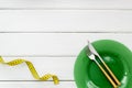 Diet concept with plate, flatware and measuring tape for weight loss on white wooden background top view mock up