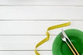 Diet concept with plate, flatware and measuring tape for weight loss on white wooden background top view mock up