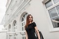 Slim pretty cheerful young woman model in a cute smile in an elegant black dress with bare shoulders with a leather black trendy Royalty Free Stock Photo