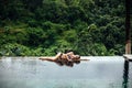 Slim brunette woman in swimsuit relaxing on edge tropical infinity pool in jungle. Palms around and crystal clean Royalty Free Stock Photo